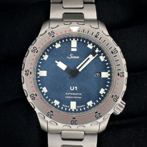 2019 Sinn U1 1010.18484 in a 44mm stainless steel case. This Sinn includes: outer box; inner case; band tool; link tool; instruction booklet; three extra links; and warranty card. The Sinn U1 is a robust German diving watch known for its case made from high-strength German submarine steel, which is highly resistant to seawater and corrosion. It is water-resistant to 1,000 meters (100 bar) and certified to European diving standards. Key features include a 44mm case, a high-contrast dial, and a crown positioned at the 4 o'clock position to avoid pressure on the back of the hand.