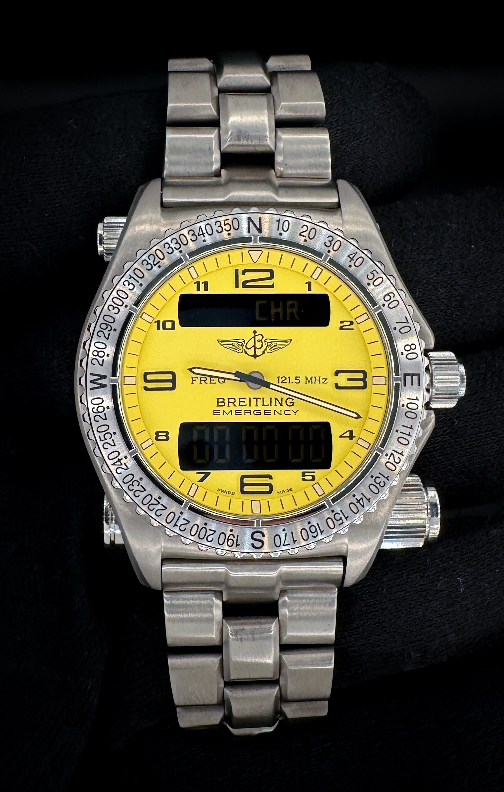 Like-New Breitling Emergency E56321 in a 43mm titanium case, powered by the Breitling 56 quartz movement. This Breitling has been tested in excellent working order with all batteries in the watch, transmitter, and tester replaced November 2025. Includes: Breitling carrying case; chronometre certificate; punched warranty booklet; hang tag; transmitter tester; screwdriver; emergency tag; instructions booklet; and sealed VHS tape.