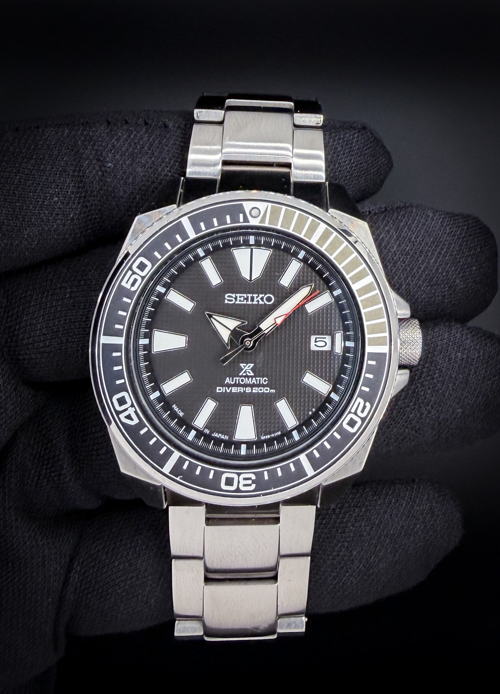 Seiko "Samurai" Prospex Diver SRPF03 in a 44mm stainless steel case, powered by the Seiko 4R35 automatic movement. This Seiko includes: Outer Sleeve, Inner Box; Hang Tag; Warranty Card; and Full Extra Links.  The Seiko SRPF03 “Samurai” is a bold, adventure-ready dive watch that combines rugged functionality with distinctive angular styling. Housed in Seiko’s signature Samurai case, the SRPF03 features sharp facets and a robust 200 m water-resistance rating, making it equally at home on land or below the waves. Its crisp black dial, large luminous hands and markers, and a unidirectional dive bezel ensure excellent legibility in low-light conditions, while the reliable automatic Seiko 4R35 movement delivers dependable performance with a hacking seconds and hand-winding capability. Finished with a comfortable stainless-steel bracelet and classic dive aesthetics, the SRPF03 Samurai is celebrated by enthusiasts for offering exceptional durability and value in the mid-range mechanical dive watch category.