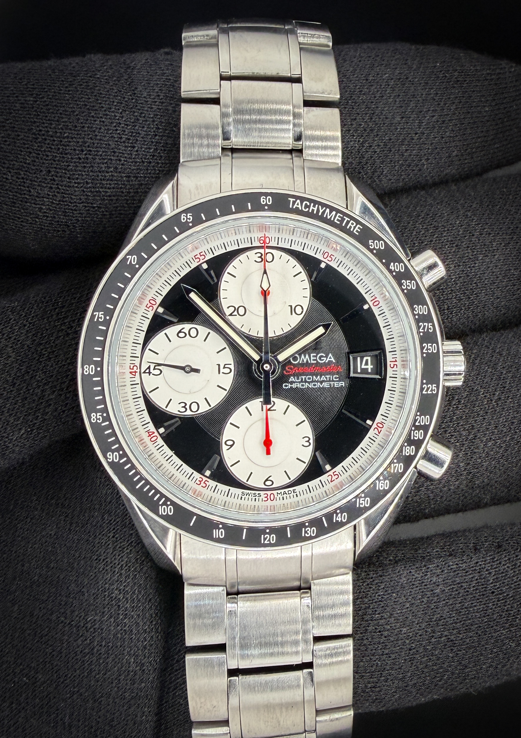 Offered here is the Omega Speedmaster Date 40mm Ref. 3210.51.00, a bold and highly legible automatic chronograph that blends classic Speedmaster DNA with modern sport styling. This example features a striking black dial with contrasting silver sub-dials in a panda-style configuration. The dial is accented with red chronograph details, including the central seconds hand and red script “Speedmaster” text, giving the watch a dynamic, motorsport-inspired presence. Applied luminous hour markers and broad arrow-style hands ensure excellent readability.