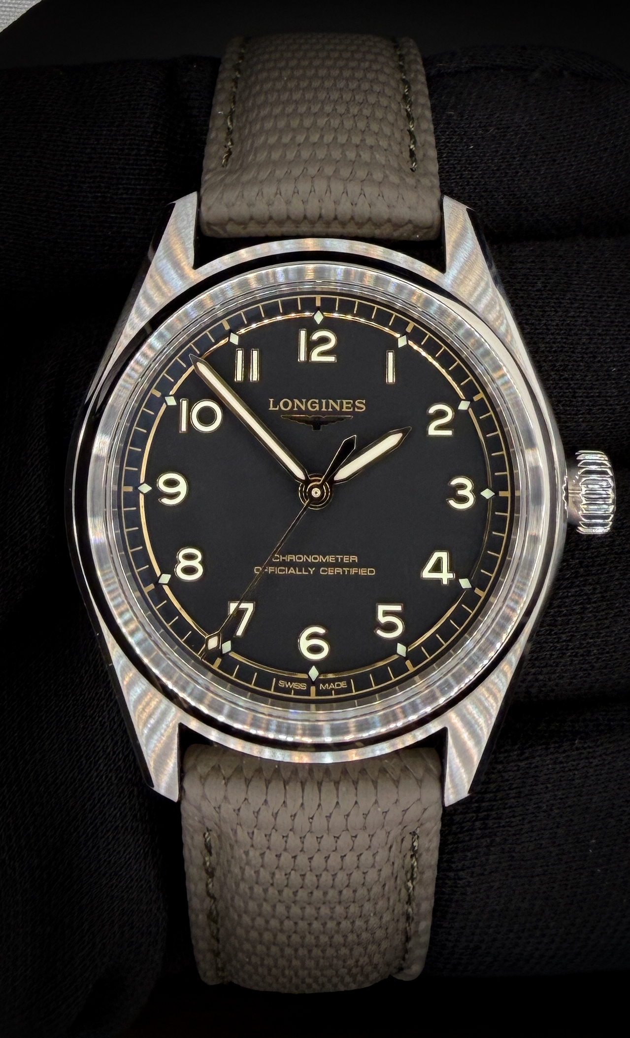 Offered here is the Longines Spirit Pilot L3.809.4.53.9, featuring a deep matte black dial with applied Arabic numerals and a warm gilt-tone minute track that gives the watch a subtle vintage aviation character. The stainless steel case measures 39mm and presents with a balanced, purposeful profile, paired here with the factory grey textile strap. The dial is signed “Chronometer Officially Certified,” and the luminous handset and numerals provide excellent legibility in all lighting conditions. This example includes the original outer box, inner presentation case, COSC Certified Chronometer card, Longines international warranty card dated 06/12/2025, instruction manual, hang tag, and polishing cloth — a complete set. The watch is running as expected for a modern COSC-certified Longines automatic movement.