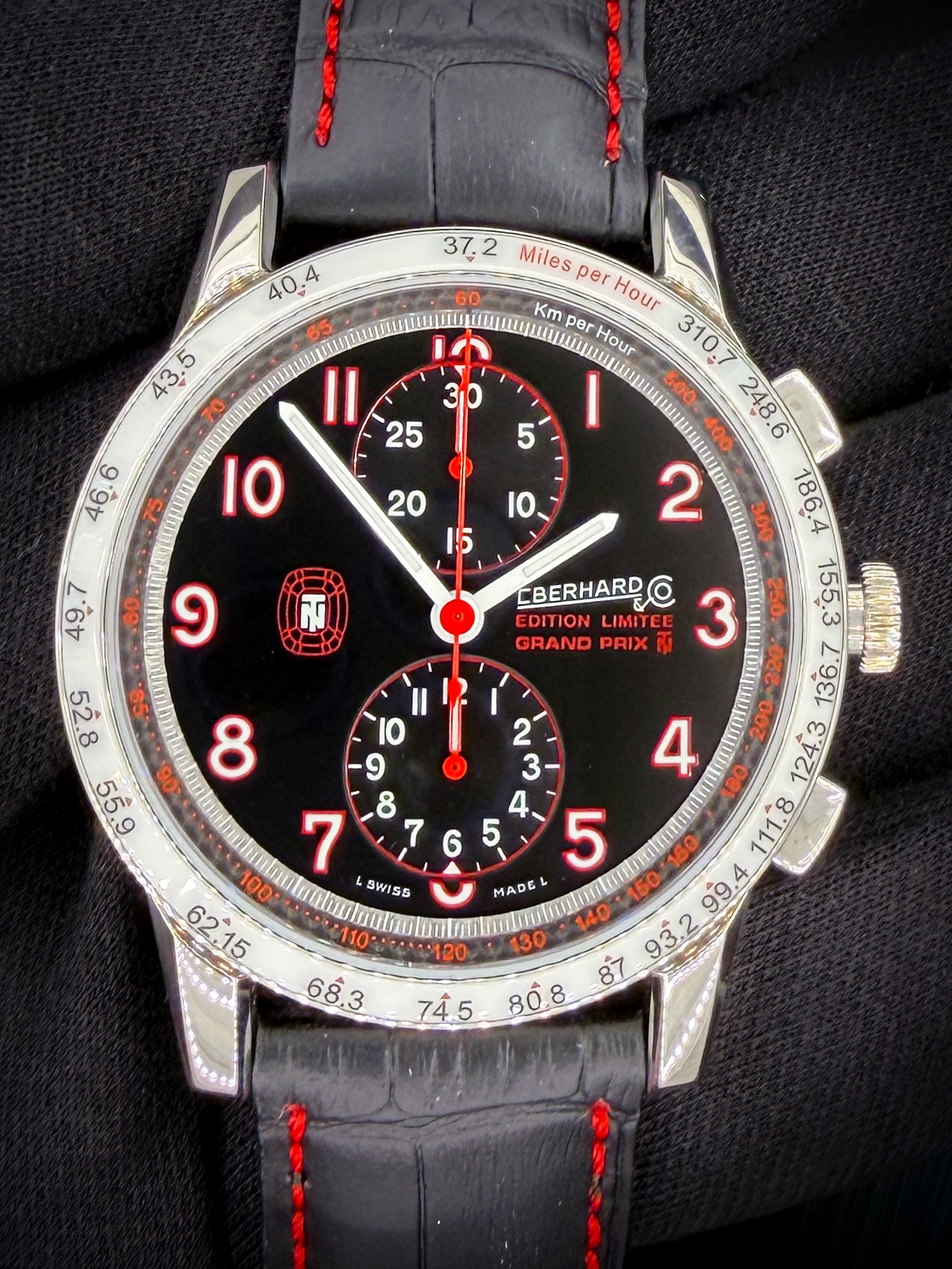 Offered here is the Eberhard & Co. Tazio Nuvolari Grand Prix Chronograph Limited Edition, limited to 999 pieces, reference 31061.1, presented in new condition. This model celebrates Eberhard’s longstanding connection to historic motorsport as the Official Timekeeper of the Gran Premio Nuvolari, an international rally honoring one of the most legendary racing drivers of all time, Tazio Nuvolari. The watch features a bold and distinctive design, highlighted by a white "MPH" bezel with red and black markers that complement the black dial with red accents. The stainless steel case measures approximately 43mm, offering a strong and sporty wrist presence. It is powered by the reliable ETA Valjoux 7750 automatic chronograph movement, delivering a power reserve of approximately 42 hours. The watch is fitted on a black leather strap with red stitching and also includes an additional black strap for versatility. This example includes the outer box, inner case, guaranty booklet, and open warranty cards dated 14 JUIL 2021.