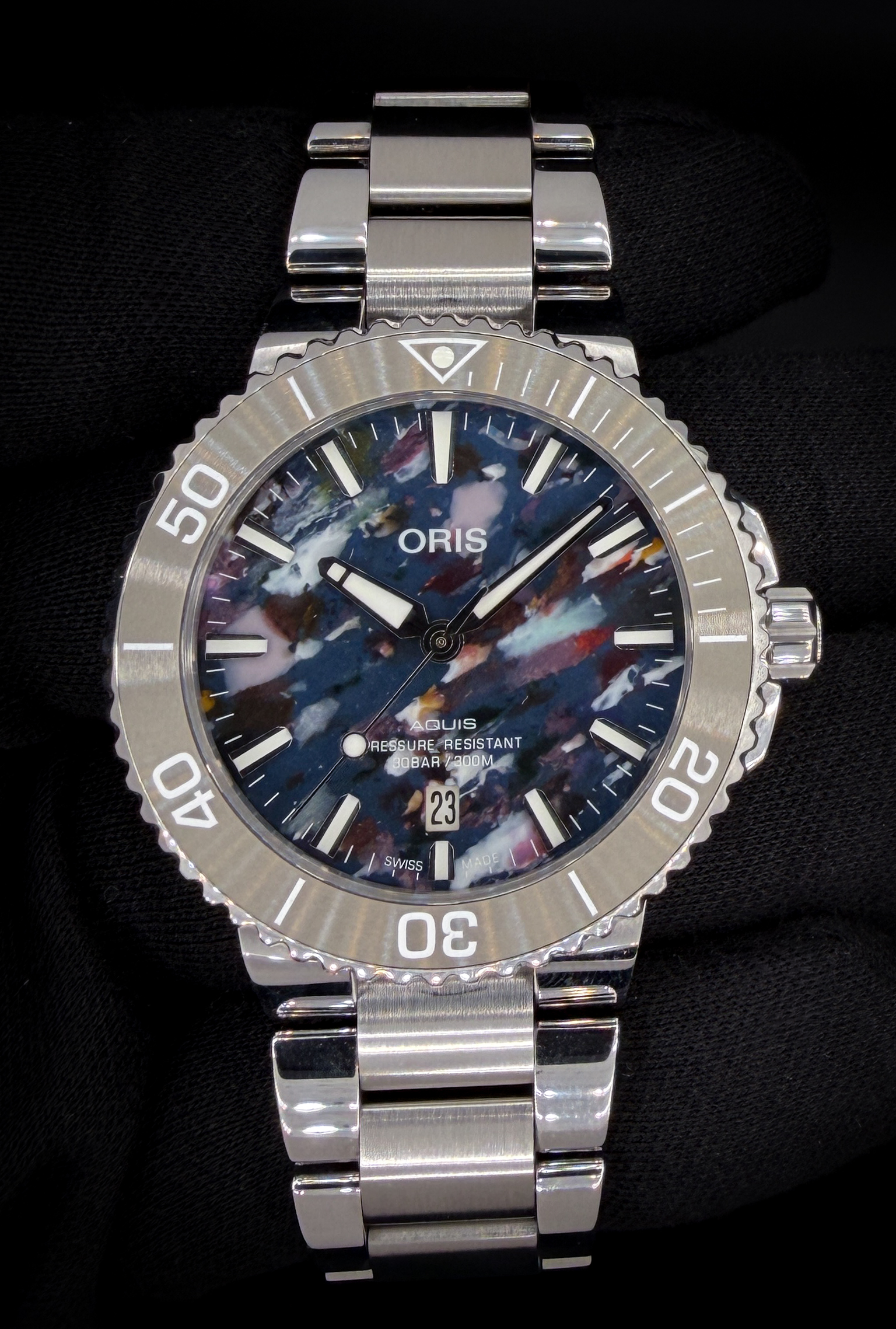 Offered here is the Oris Aquis Date “Upcycle” reference 01 733 7766 4150, a distinctive modern dive watch known for its sustainability-focused design and one-of-a-kind dial. Each “Upcycle” dial is crafted from recycled ocean plastic, resulting in a unique multicolor pattern—no two dials are exactly alike—while still maintaining excellent legibility with applied indices and a date display at 6 o’clock. The stainless steel case measures approximately 41.5mm and is paired with a unidirectional rotating bezel, making it equally suited for daily wear or active use. Accuracy Testing: +/- 5 SPD / 307 Amplitude / .1ms Beat Error