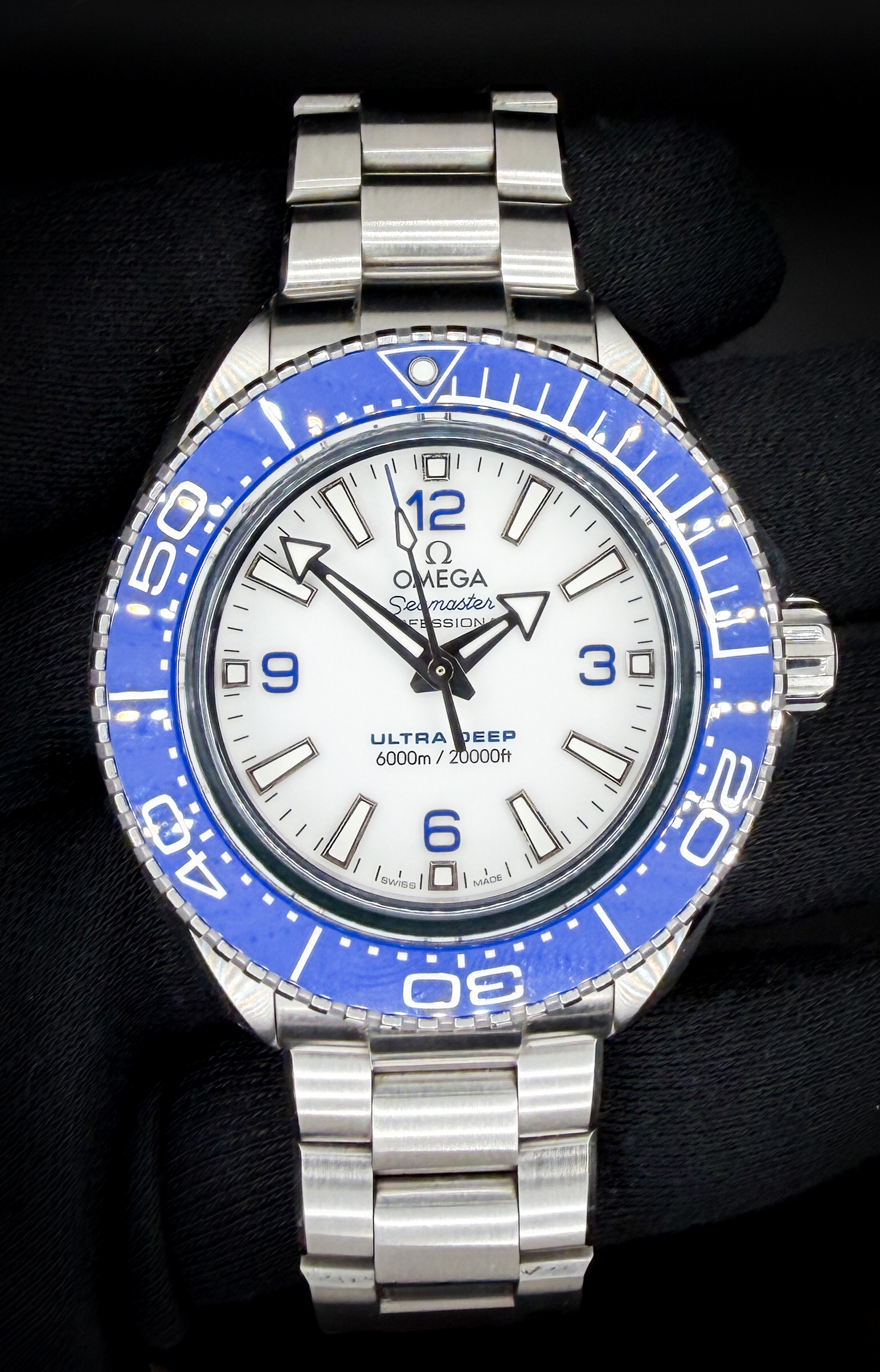 Omega Seamaster Planet Ocean Ultra Deep 216.30.46.21.04.001 in a 45.5mm stainless steel case, powered by the Omega caliber 8912 Master Chronometer movement. This reference represents Omega’s most extreme production dive watch, derived directly from the record-setting Ultra Deep prototypes that reached the Challenger Deep. This example features the highly desirable white dial configuration with bold blue Arabic numerals and matching blue ceramic bezel, creating a striking and highly legible contrast. The dial is clean and crisp, with broad arrow hands and applied indices filled with luminous material for excellent underwater visibility.