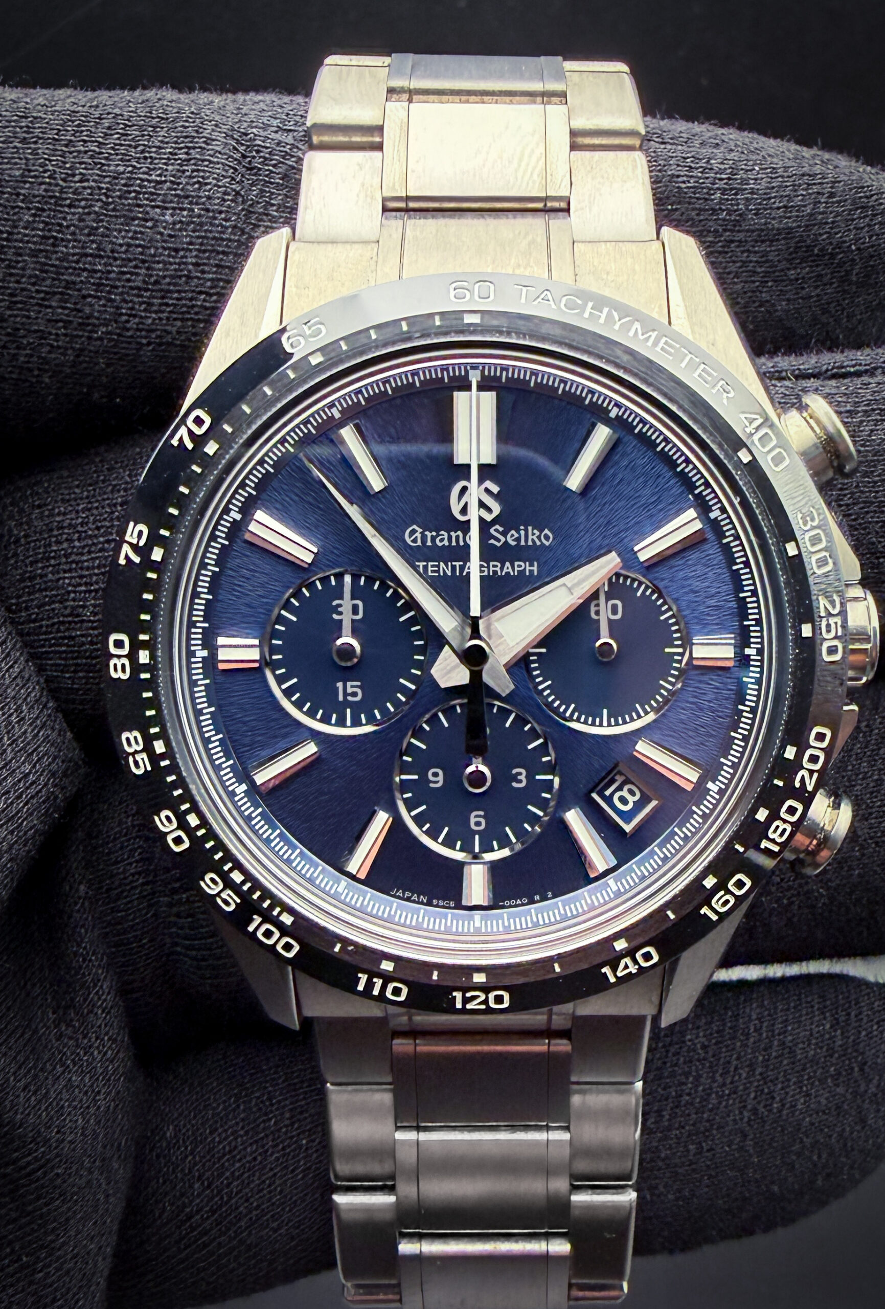 Grand Seiko Tentagraph SLGC001 in a high-intensity titanium case measuring approximately 43.2mm in diameter, representing Grand Seiko’s first fully mechanical chronograph and one of the brand’s most technically advanced sport watches to date. The Tentagraph draws clear inspiration from the legendary design language established by the Grand Seiko Evolution 9 Collection, combining razor-sharp Zaratsu polishing, deeply textured dial work inspired by Mount Iwate, and an aggressively faceted case architecture that reflects both Japanese industrial precision and modern luxury sports chronograph design. While unmistakably Grand Seiko in execution, collectors often note parallels to elite integrated luxury chronographs from brands such as Audemars Piguet and Zenith through its combination of titanium construction, high-beat movement technology, and technical finishing.