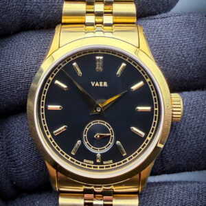 VAER A12 Ceremony in a 36mm gold-plated stainless steel case, paired with the matching VAER gold-plated Jubilee-style bracelet with a versatile 20mm lug width, delivering a refined vintage-inspired aesthetic with modern everyday wearability. The design of the A12 Ceremony openly draws inspiration from the legendary Patek Philippe Calatrava Ref. 96, with VAER specifically citing the rare black-and-gold Calatrava models of the 1940s as the foundation for the Ceremony’s minimalist dial layout, elegant proportions, and understated luxury styling. Powering the watch is the Swiss Sellita SW200-1 automatic movement, a respected caliber known for its reliability, smooth sweep seconds, and long-term serviceability. Blending classic Calatrava-inspired dress watch design with contemporary specifications such as robust construction and modern bracelet versatility, the A12 Ceremony offers an accessible interpretation of one of the most iconic dress watch aesthetics ever produced.