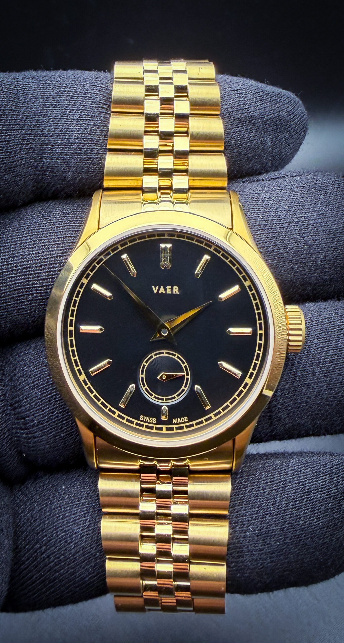 VAER A12 Ceremony in a 36mm gold-plated stainless steel case, paired with the matching VAER gold-plated Jubilee-style bracelet with a versatile 20mm lug width, delivering a refined vintage-inspired aesthetic with modern everyday wearability. The design of the A12 Ceremony openly draws inspiration from the legendary Patek Philippe Calatrava Ref. 96, with VAER specifically citing the rare black-and-gold Calatrava models of the 1940s as the foundation for the Ceremony’s minimalist dial layout, elegant proportions, and understated luxury styling. Powering the watch is the Swiss Sellita SW200-1 automatic movement, a respected caliber known for its reliability, smooth sweep seconds, and long-term serviceability. Blending classic Calatrava-inspired dress watch design with contemporary specifications such as robust construction and modern bracelet versatility, the A12 Ceremony offers an accessible interpretation of one of the most iconic dress watch aesthetics ever produced.