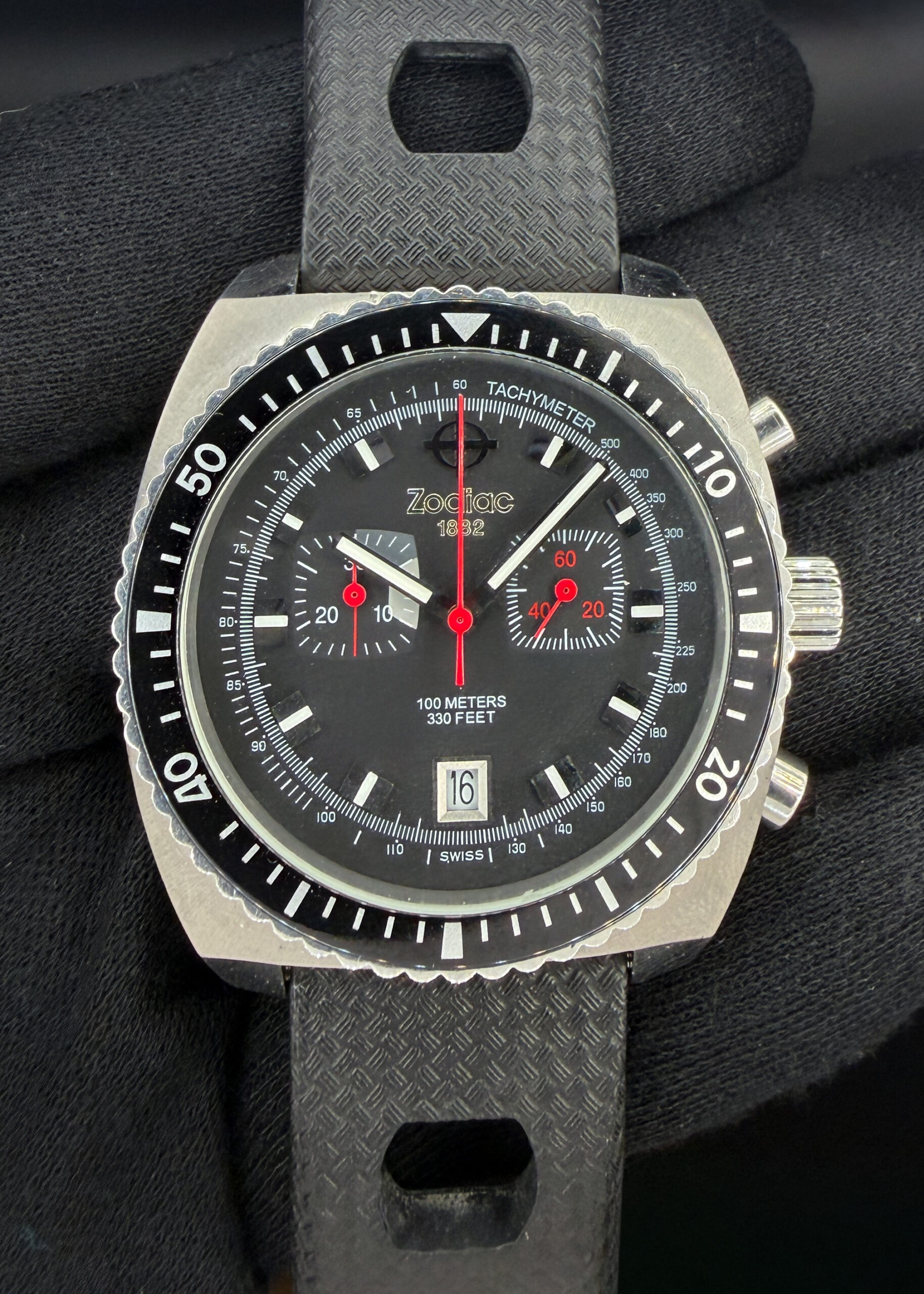 The Zodiac Sea Dragon Chronograph ZS2240 (ZO2240) combines bold 1970s styling with the precision and convenience of a Ronda 5021.D quartz movement. Its approximately 43mm stainless steel cushion case frames a black dial with twin recessed subdials, bright red timing accents, luminous hands and hour markers, and a date window at six o’clock. A black rotating timing bezel and an inner tachymeter scale reinforce its sporting character, while the movement provides a 30-minute chronograph and separate running seconds. Originally rated for 100 meters of water resistance, the Sea Dragon pairs brushed steel surfaces with polished details and a textured black rubber strap, delivering distinctive vintage appeal in a practical everyday chronograph.