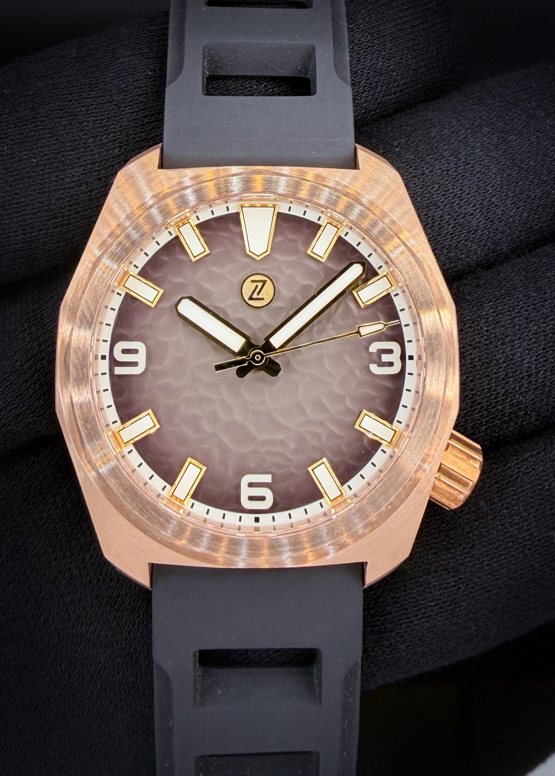Zelos Hammerhead 43 Field Bronze “Bedrock” – Limited Edition #053/150 The Zelos Hammerhead Field “Bedrock” combines a hammered brown fumé dial with a warm CuSn8 bronze case that develops its own patina over time. Bold luminous hands, applied hour markers, and prominent Arabic numerals at three, six, and nine provide clear legibility against the textured dial. Its 43mm cushion-shaped case measures 48mm from lug to lug and features a domed sapphire crystal with an internal anti-reflective coating. Powered by the Seiko NH38 automatic movement, this model offers a clean display without a date and a factory water-resistance rating of 300 meters. The original black FKM rubber strap features a matching bronze buckle.