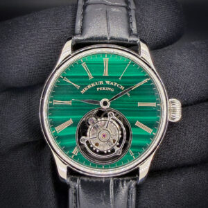 Merkur Watch Co. Peking Tourbillon — Green Malachite Dial — 42mm The Merkur Watch Co. Peking Tourbillon combines a richly banded green malachite dial with gold-tone Roman numerals, polished hands, and a prominently displayed tourbillon at 6 o’clock. The polished stainless steel case measures 42mm in diameter, approximately 12.5mm thick, and 48mm lug-to-lug. Powered by a hand-wound mechanical tourbillon movement, this watch offers a compelling view of its mechanics from both sides. The exhibition caseback reveals the skeletonized bridges and exposed gear train, while a sapphire crystal protects the dial. A black embossed leather strap completes its classic dress-watch presentation. This example is new and includes the travel case, polishing cloth, and instruction book.