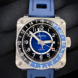 Aquatico Steel Man GMT Blue Automatic — #433/999 — Box & Papers The Aquatico Steel Man GMT pairs a bold square stainless steel case with a blue sunburst dial, contrasting black chapter ring, and blue-and-black 24-hour bezel. Large Arabic numerals, luminous hands, and a red-tipped GMT hand give the watch a distinctive, easy-to-read layout. The case measures 43mm wide, 15.5mm thick, and 50mm lug-to-lug. Inside is a Japanese Seiko NH34A automatic movement with date display and an independently adjustable GMT hand for tracking a second time zone. Sapphire crystal, an exhibition caseback, and a screw-down crown complete the construction. The model carries a manufacturer-rated water resistance of 1,000 meters. Numbered 433/999, this example is presented in new condition and fitted with a blue rubber strap. Includes the outer sleeve, outer box, inner wooden presentation case, instruction card, warranty card dated June 26, 2025, and an additional unworn brown leather strap.