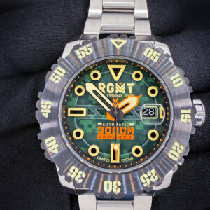 RGMT Ohio Automatic “Army Green” RG-8034-0K – Limited Edition #009/100 The RGMT Ohio “Army Green” combines a green digital camouflage dial with bold luminous hour markers, contrasting orange accents, and a substantial 45mm stainless steel case. Named after the U.S. Navy’s Ohio-class submarines, this model features a Japanese automatic movement, magnified date display at three o’clock, sapphire crystal, and screw-down crown. Its deeply notched dive bezel features luminous markings, while the stainless steel bracelet completes its rugged appearance. The Ohio carries a factory water-resistance rating of 3,000 meters.