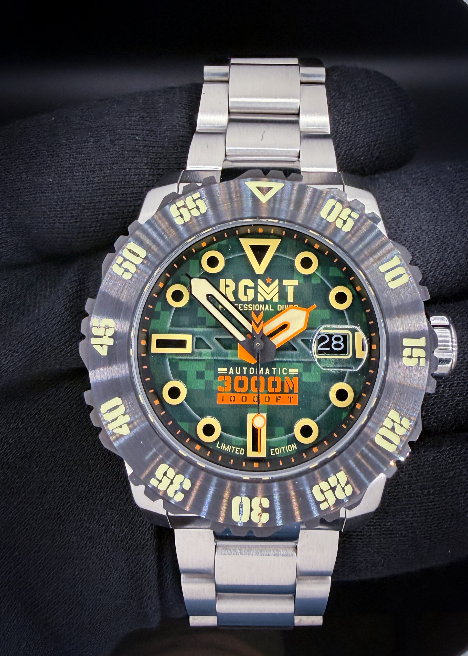 RGMT Ohio Automatic “Army Green” RG-8034-0K – Limited Edition #009/100 The RGMT Ohio “Army Green” combines a green digital camouflage dial with bold luminous hour markers, contrasting orange accents, and a substantial 45mm stainless steel case. Named after the U.S. Navy’s Ohio-class submarines, this model features a Japanese automatic movement, magnified date display at three o’clock, sapphire crystal, and screw-down crown. Its deeply notched dive bezel features luminous markings, while the stainless steel bracelet completes its rugged appearance. The Ohio carries a factory water-resistance rating of 3,000 meters.